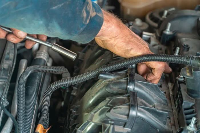 Mani del meccanico al lavoro su un motore con la chiave a bussola