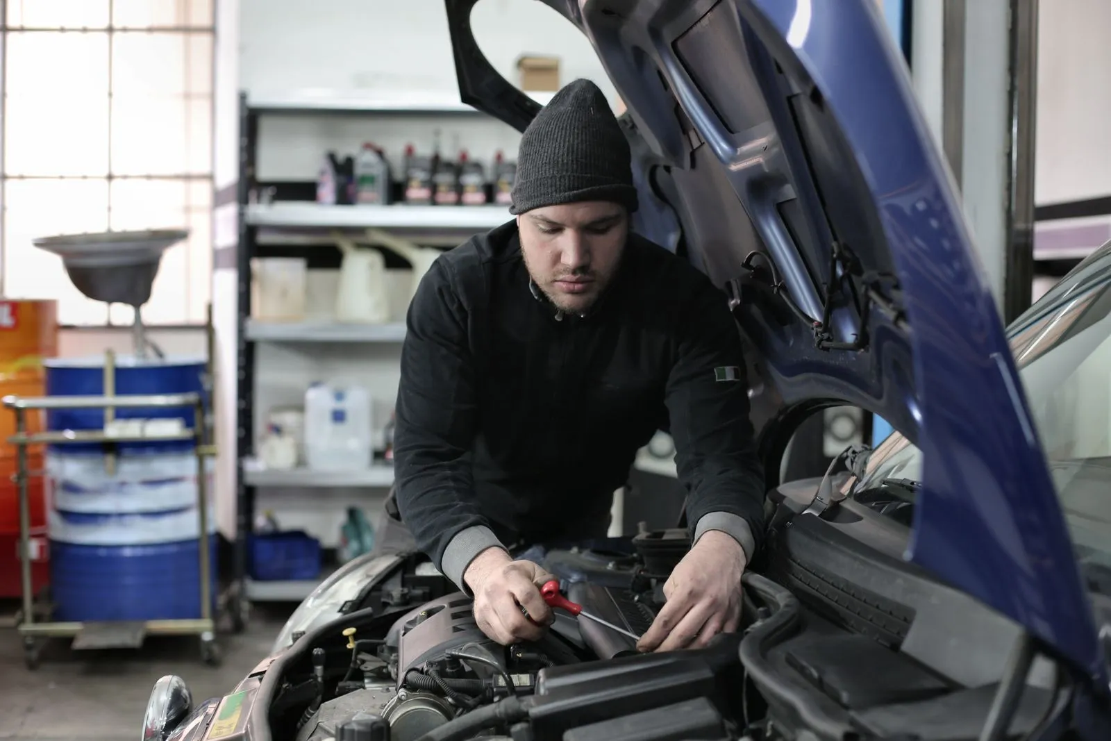 Meccanico dell'officina al lavoro nel vano motore di un'auto blu, concentrato con l'attrezzo in mano